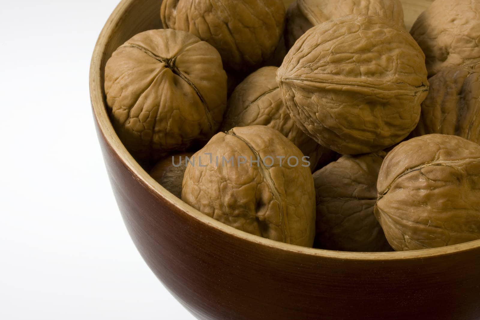 a wooden bowl of walnuts against white background, copy space
