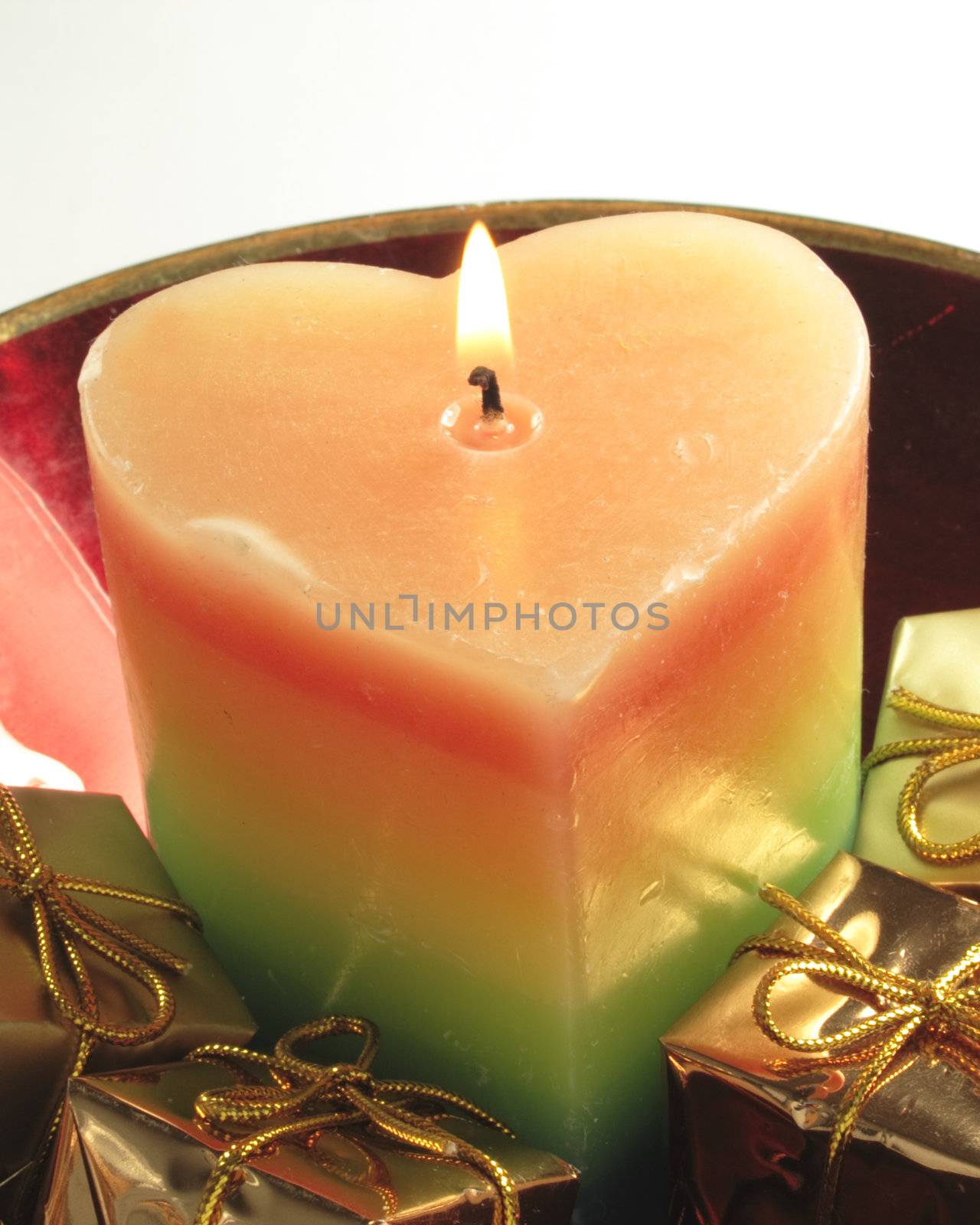 heart shaped candle and gold presents in a red glass bowl