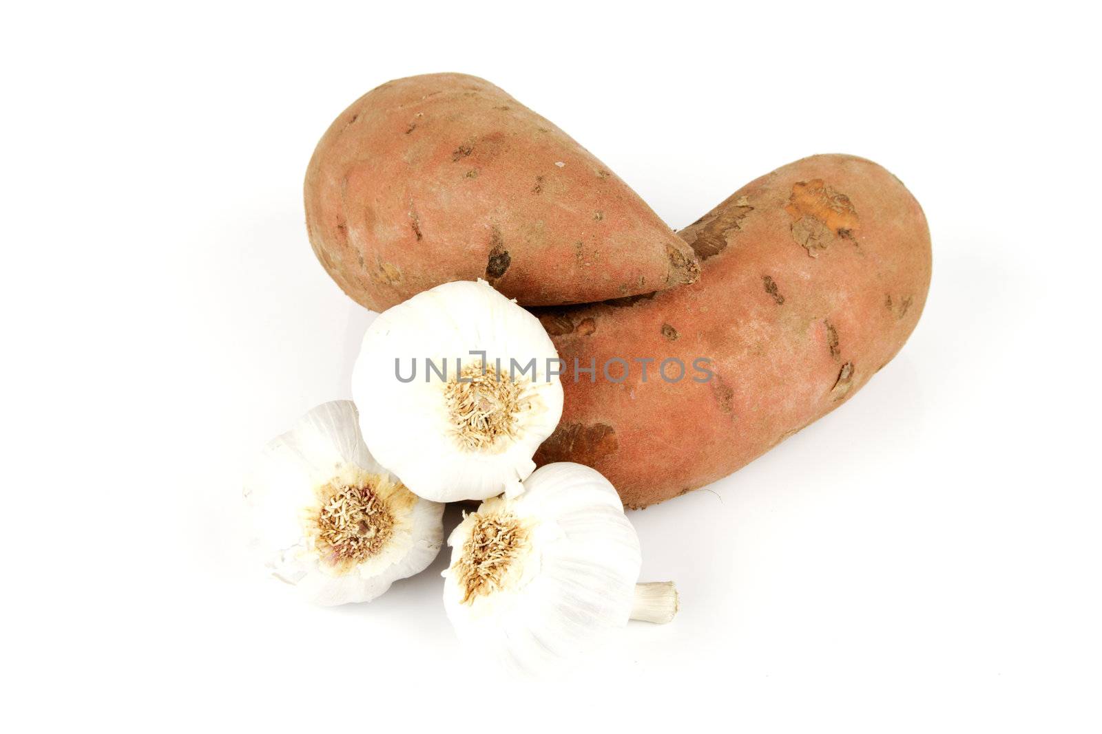 Two raw unpeeled sweet potatoes with white garlic bulbs on a reflective white background