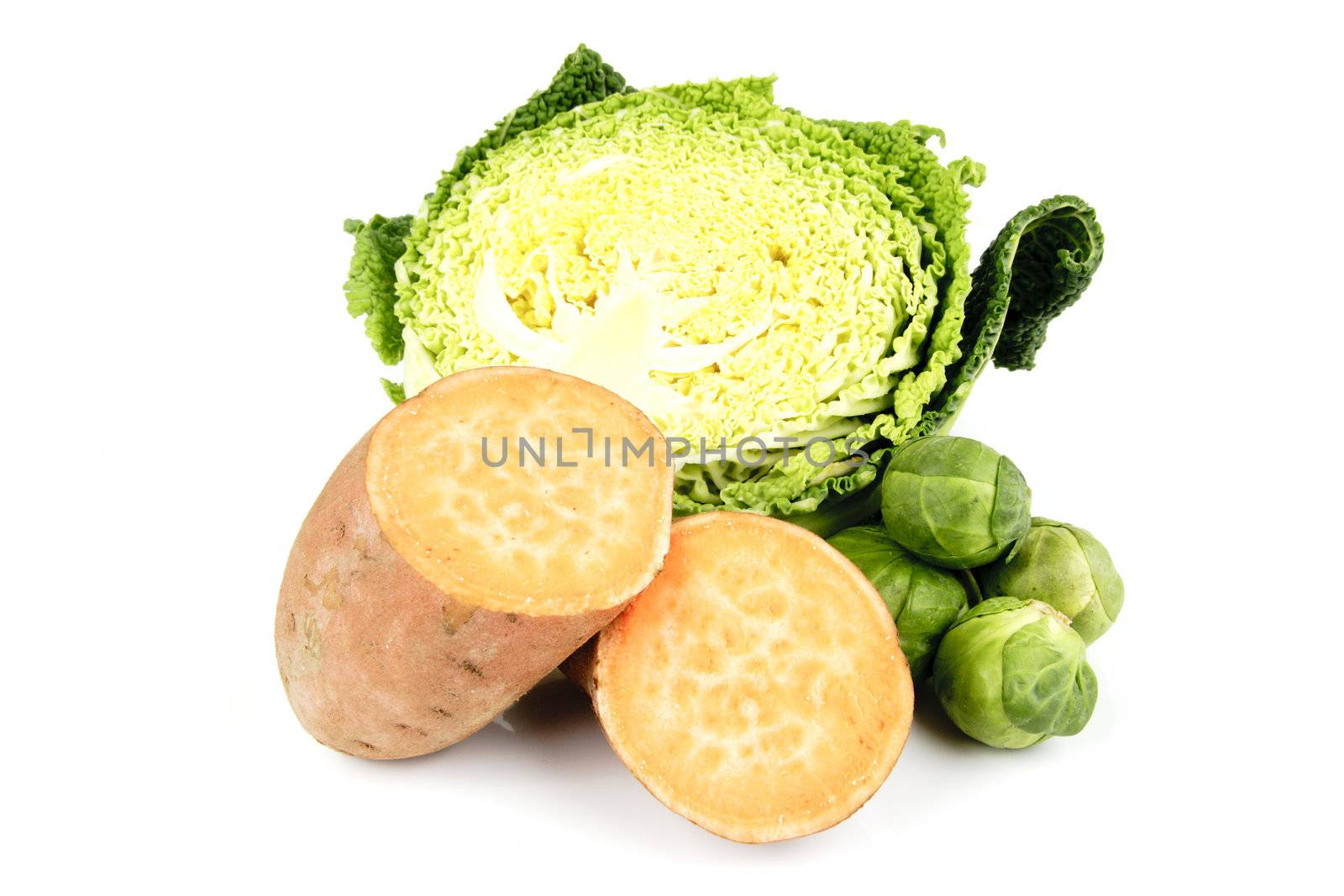 Half a raw green cabbage with a sweet potato cut in half and a pile of green sprouts on a reflective white background