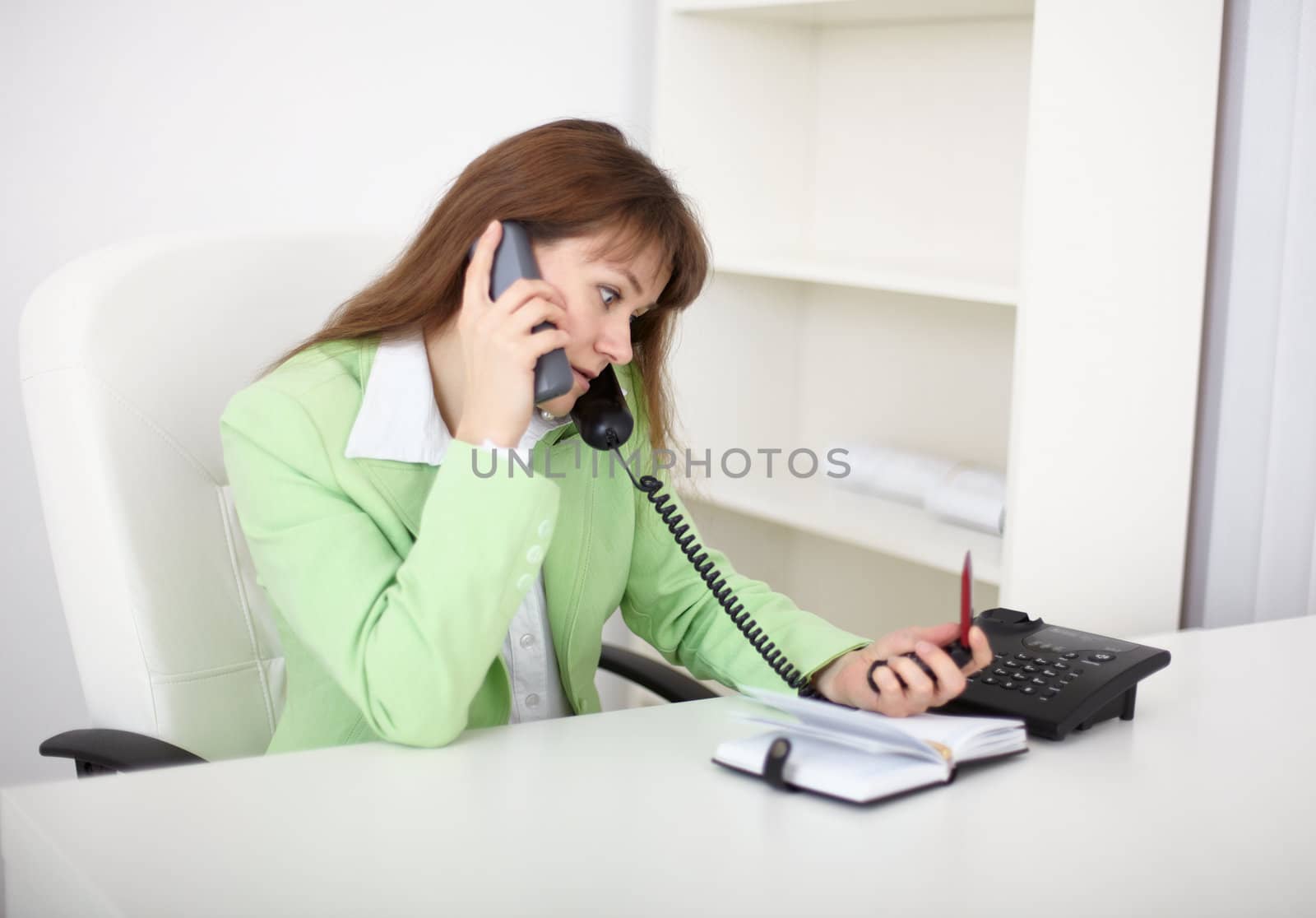 One girl is sitting at desks and talking on the phone