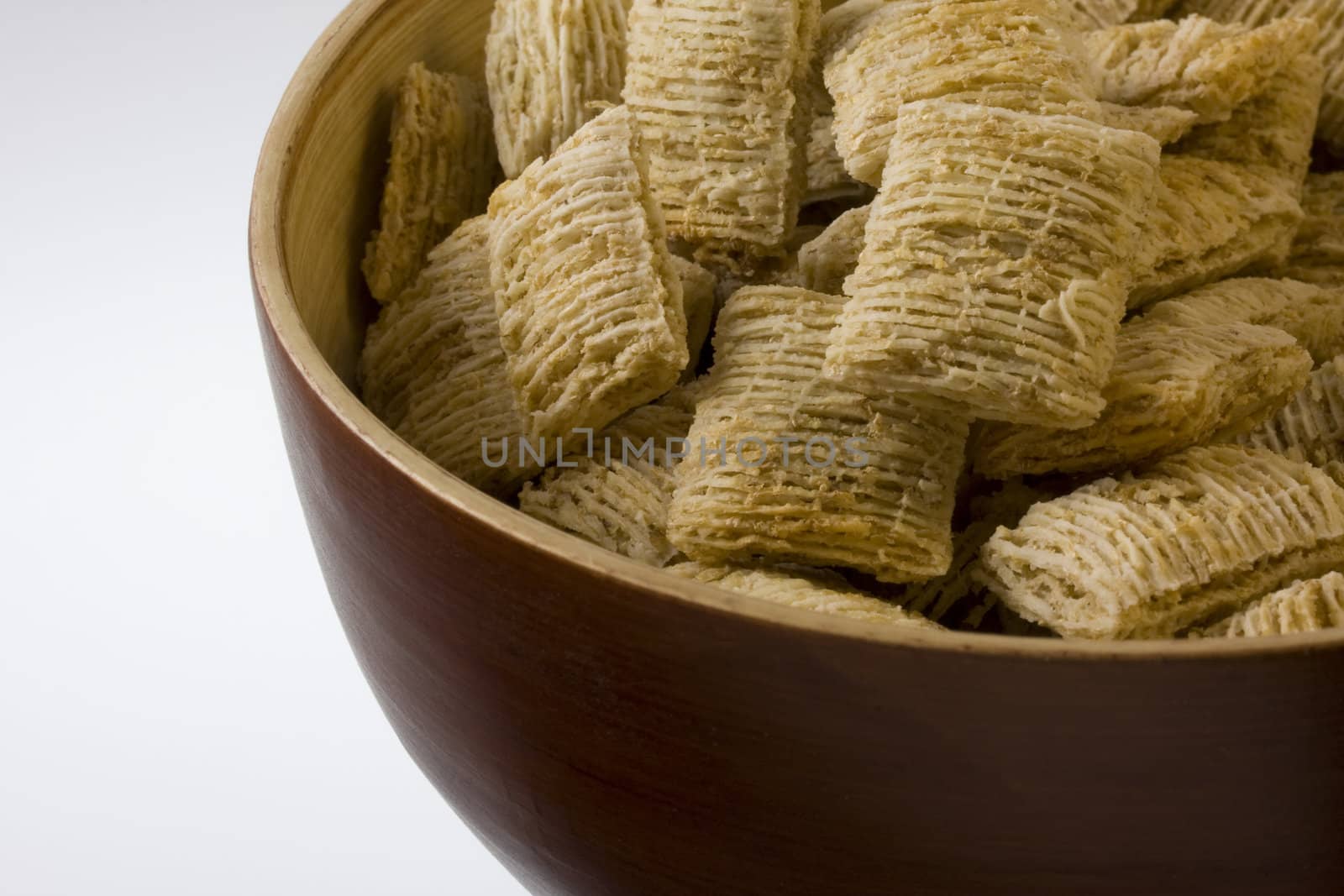 a wooden, round, bowl of shredded wheat cereal (dry, no milk), white copy space