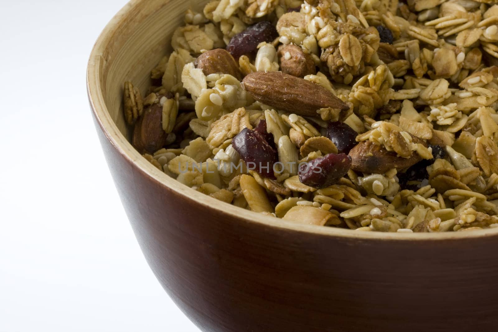 a wooden bowl of dry (no milk) natural granola with cranberries almonds, and other nuts; white copy space