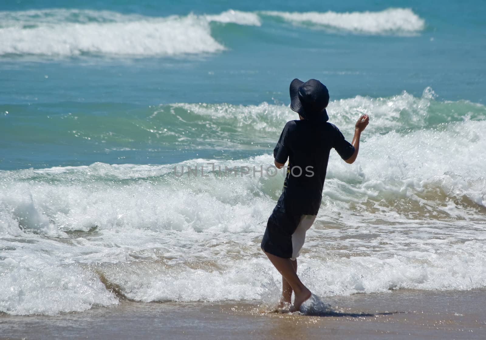 a boy stops in front of waves at the beach