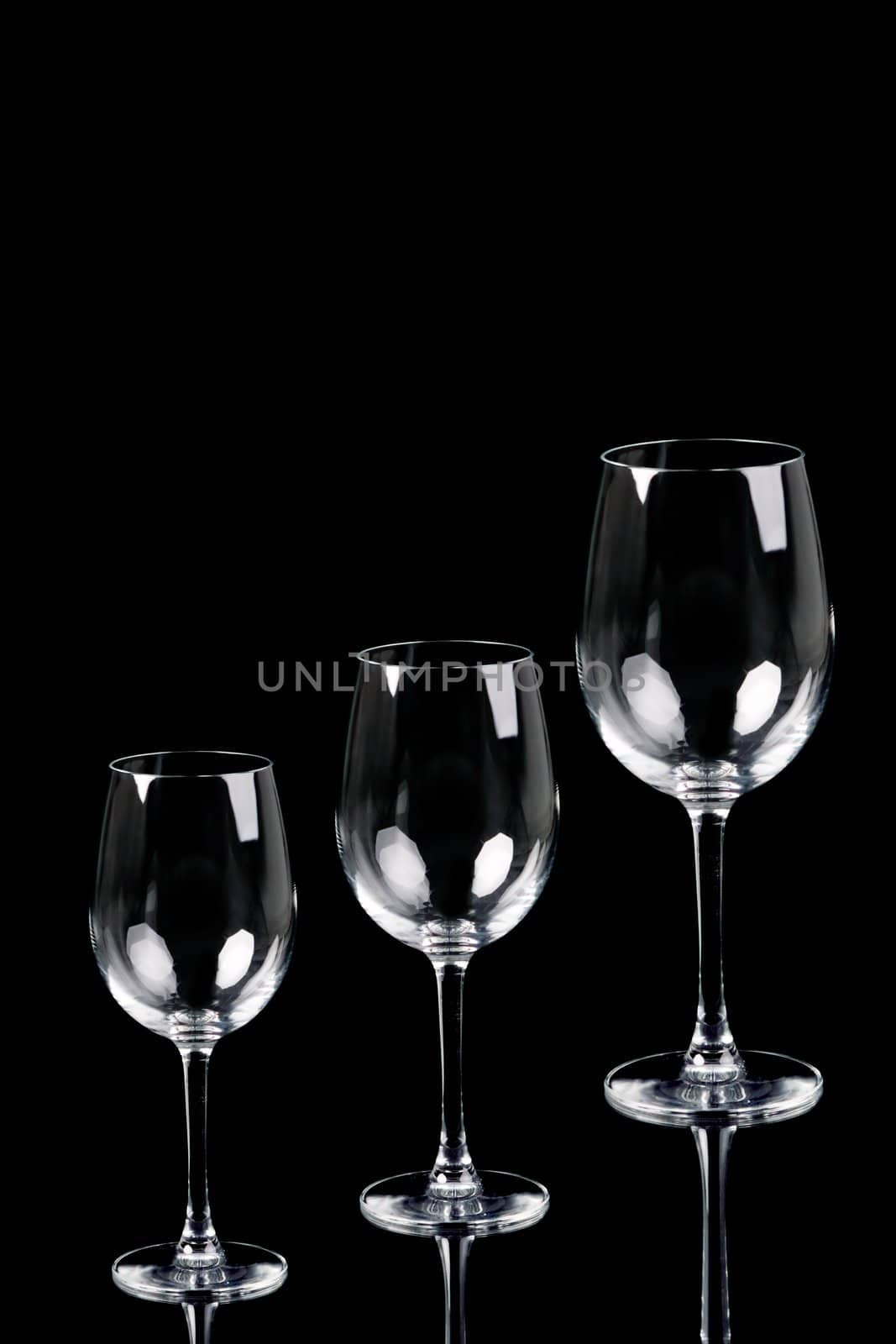 Three empty glasses over black background with reflection. Water, white wine and red wine.