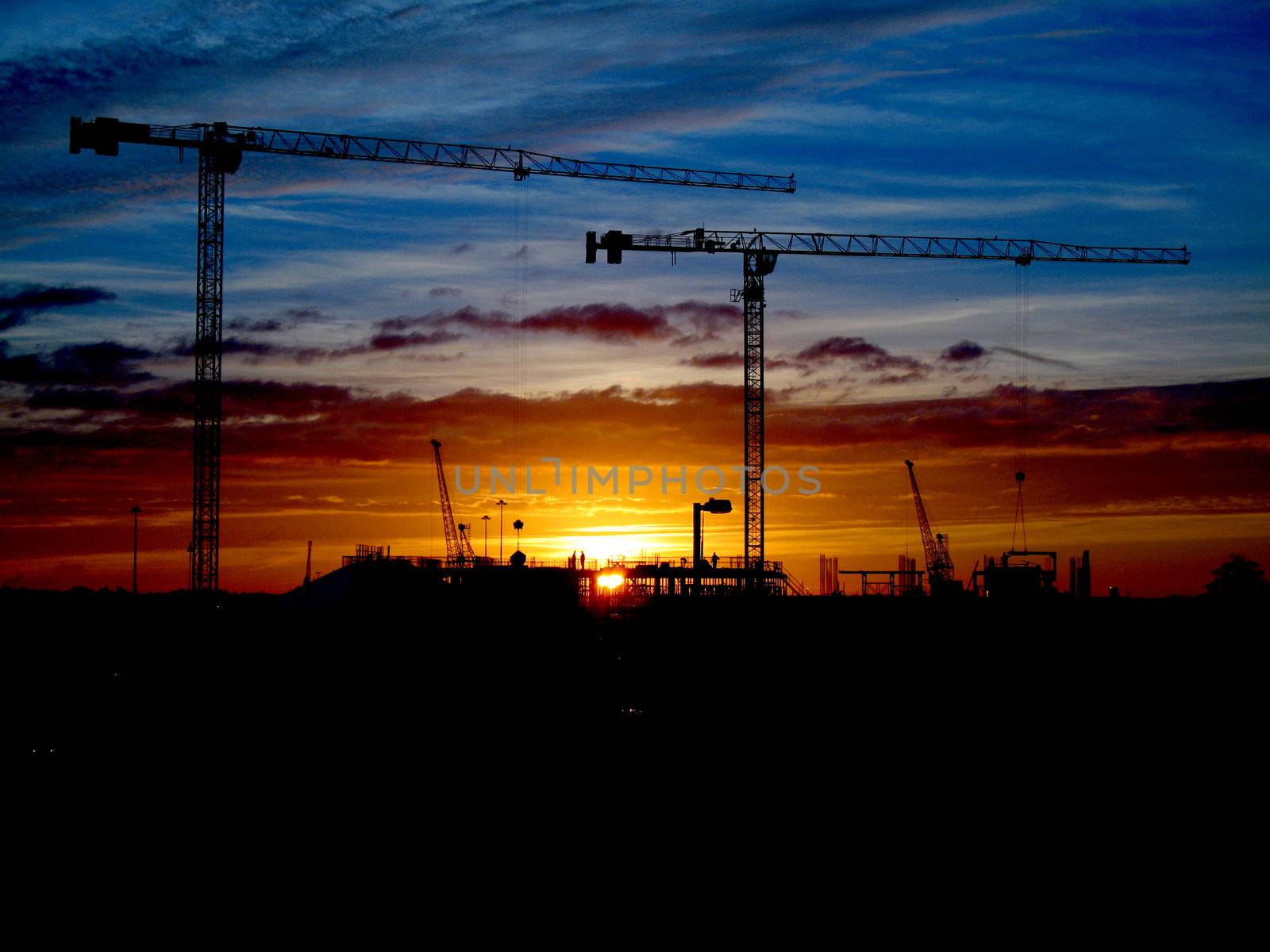 Cranes and construction site silhouette against setting (or rising) sun