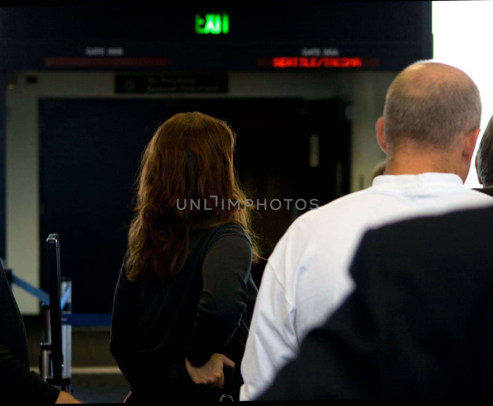 Female Airline Passenger is standing in line as she prepares to board her departing flight aboad a plane. The light is casting a nice Aura about her red hair.
