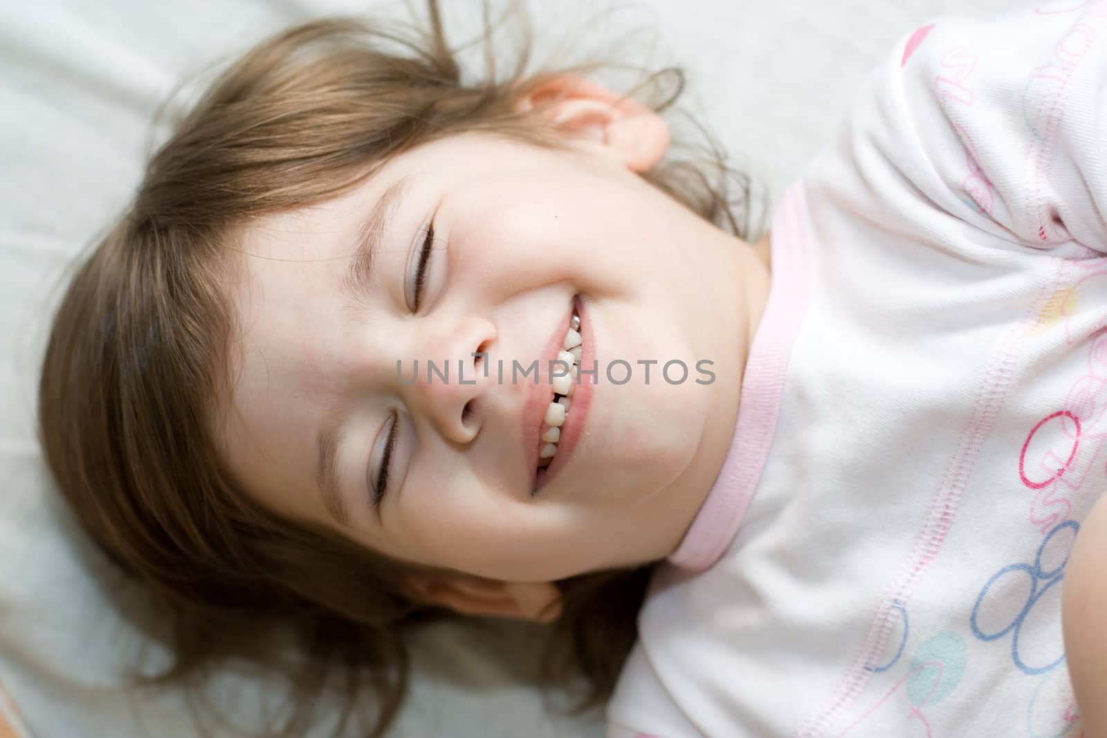 3-year-old happy girl with closed eyes lying in bed and smiling