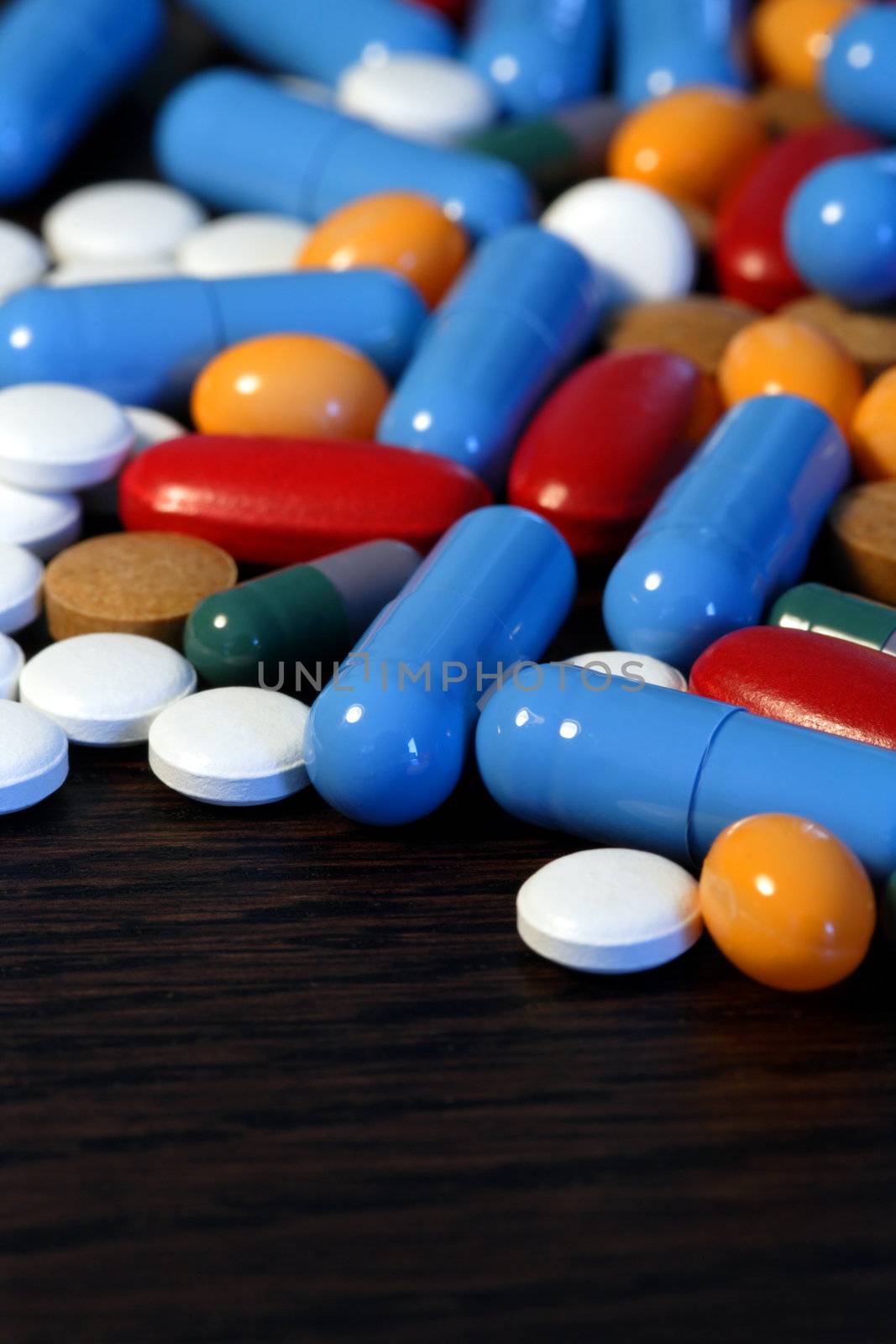 Collection of assorted pills on a dark wood table. Shallow depth-of-field.
