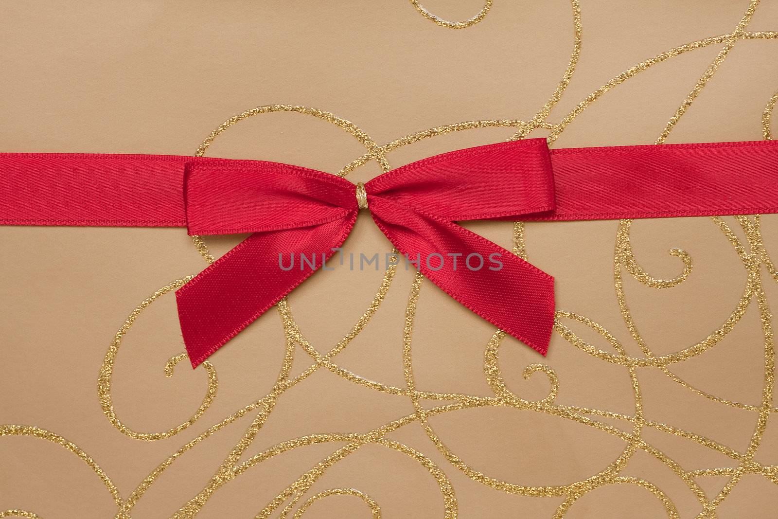 Detail of a parcel wrapped with gold paper and decorated with red ribbon.