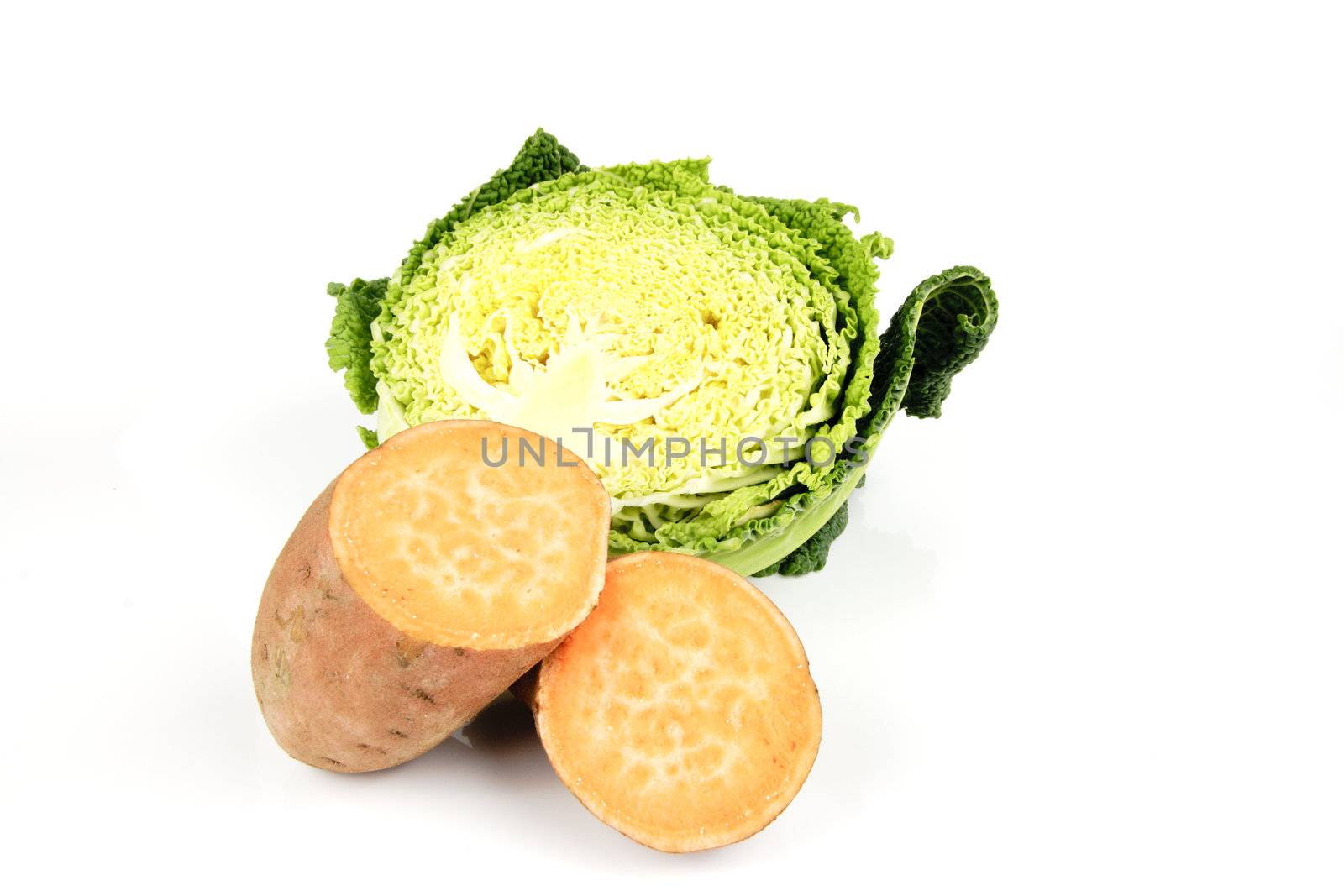 Half a raw green cabbage with a sweet potato cut in half on a reflective white background