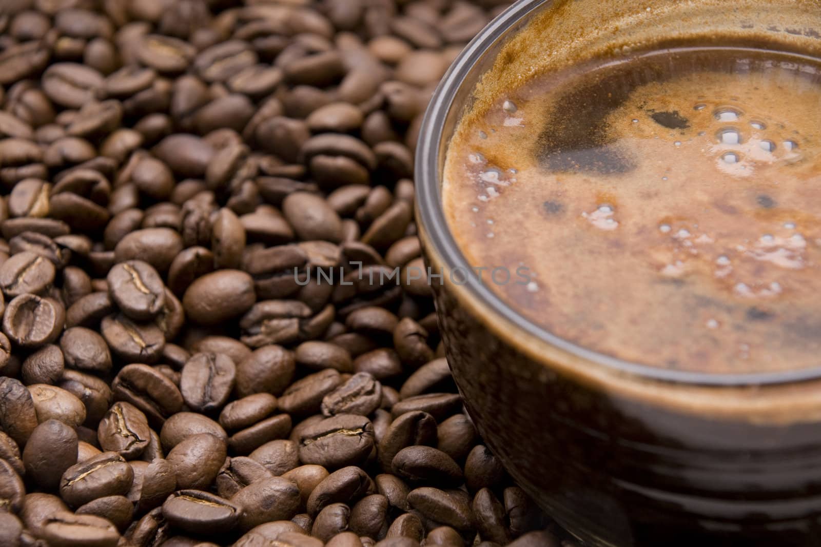 cup of espresso with froth surrounded by coffee beans