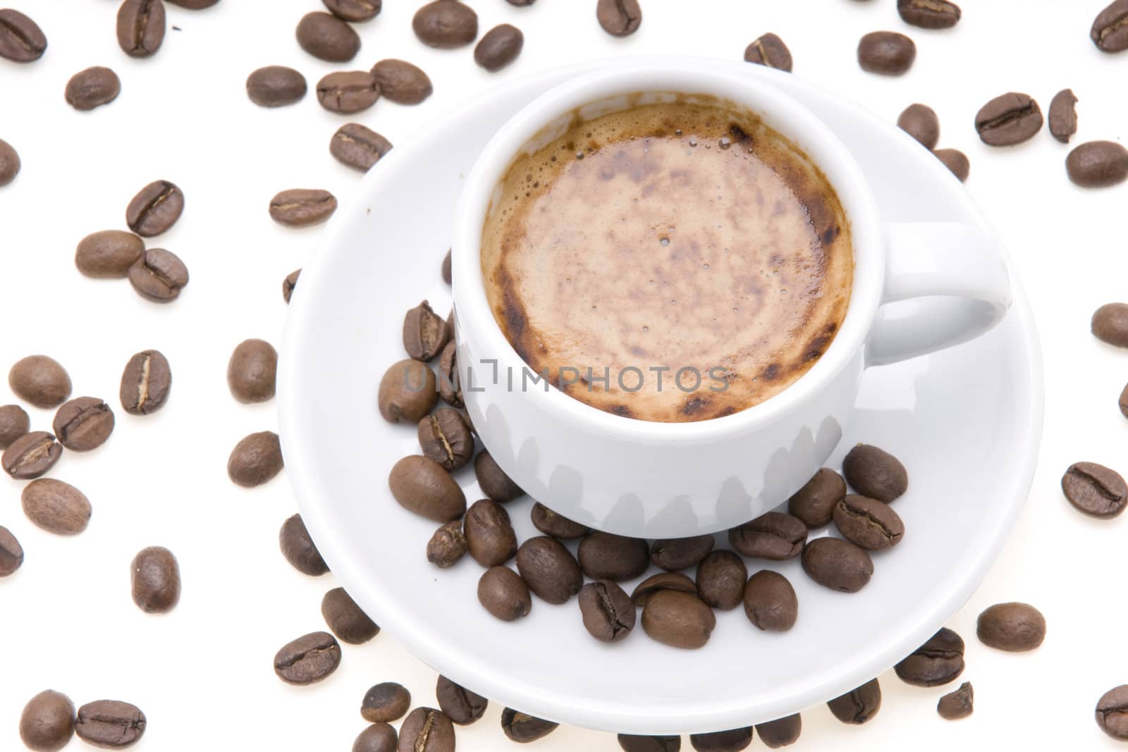 cup of espresso with froth surrounded by coffee beans