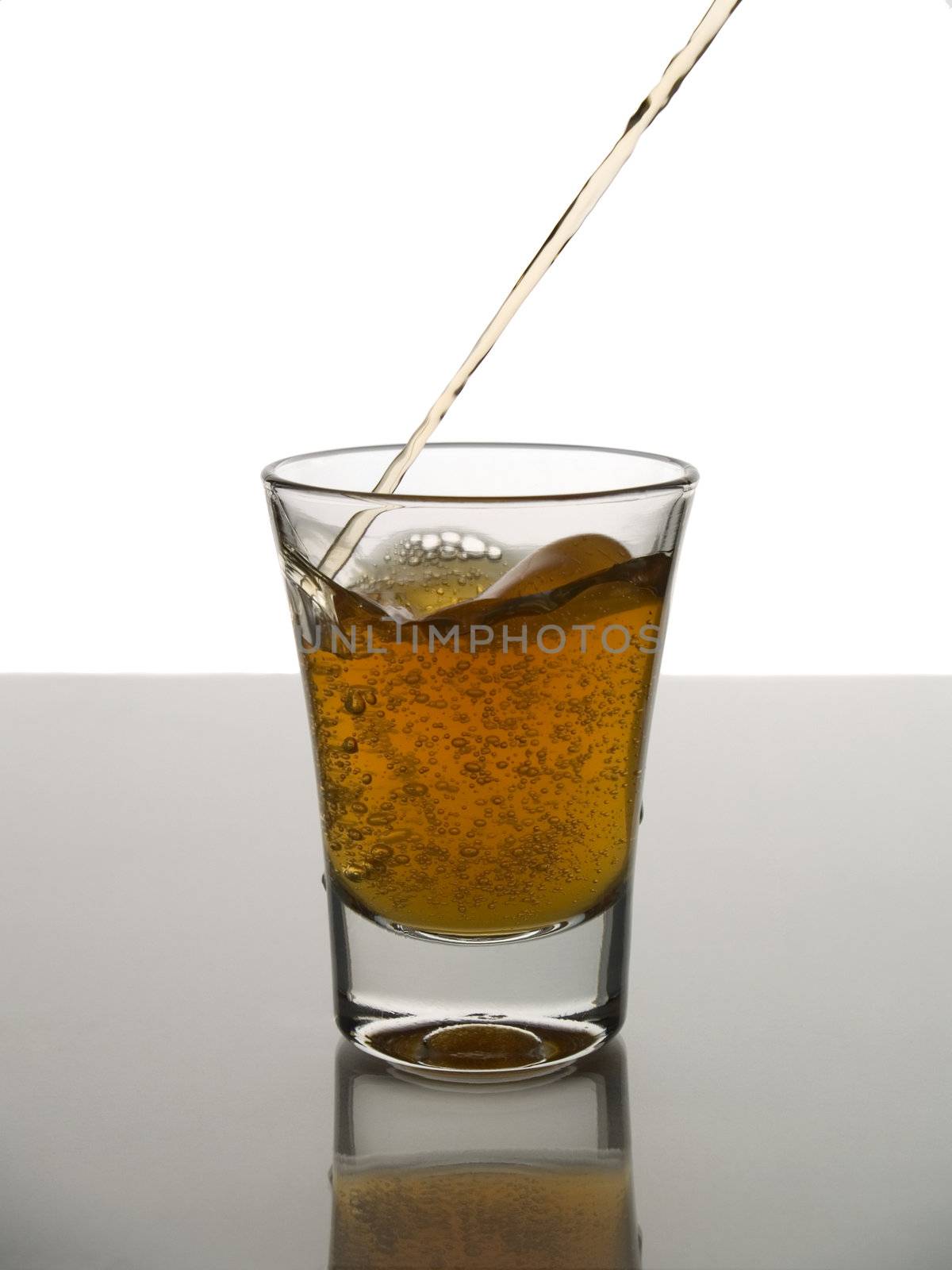 Pouring a shot of whisky on white background over gray floor.