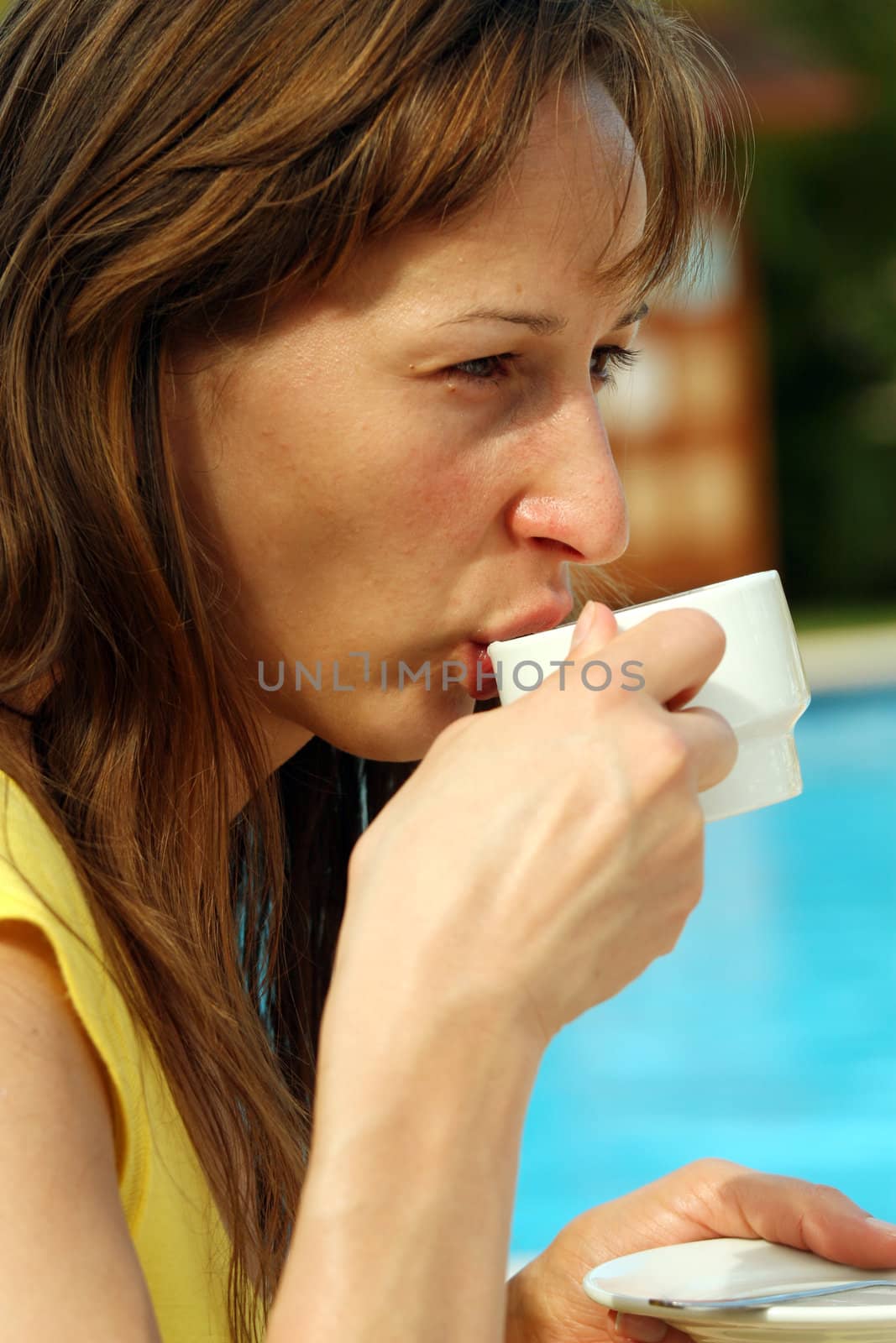Woman drinking a cup coffee by the pool