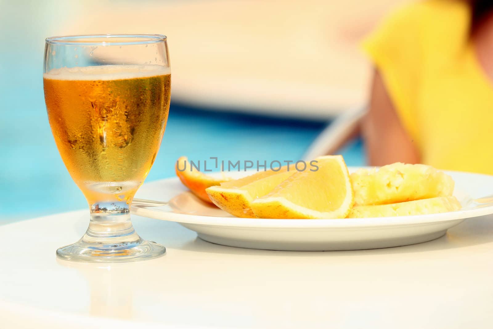 Glass beer and tasty fruits on the table by the pool