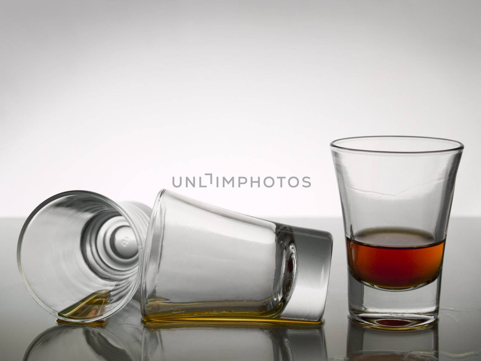 Three shots of whisky on white background over gray floor.