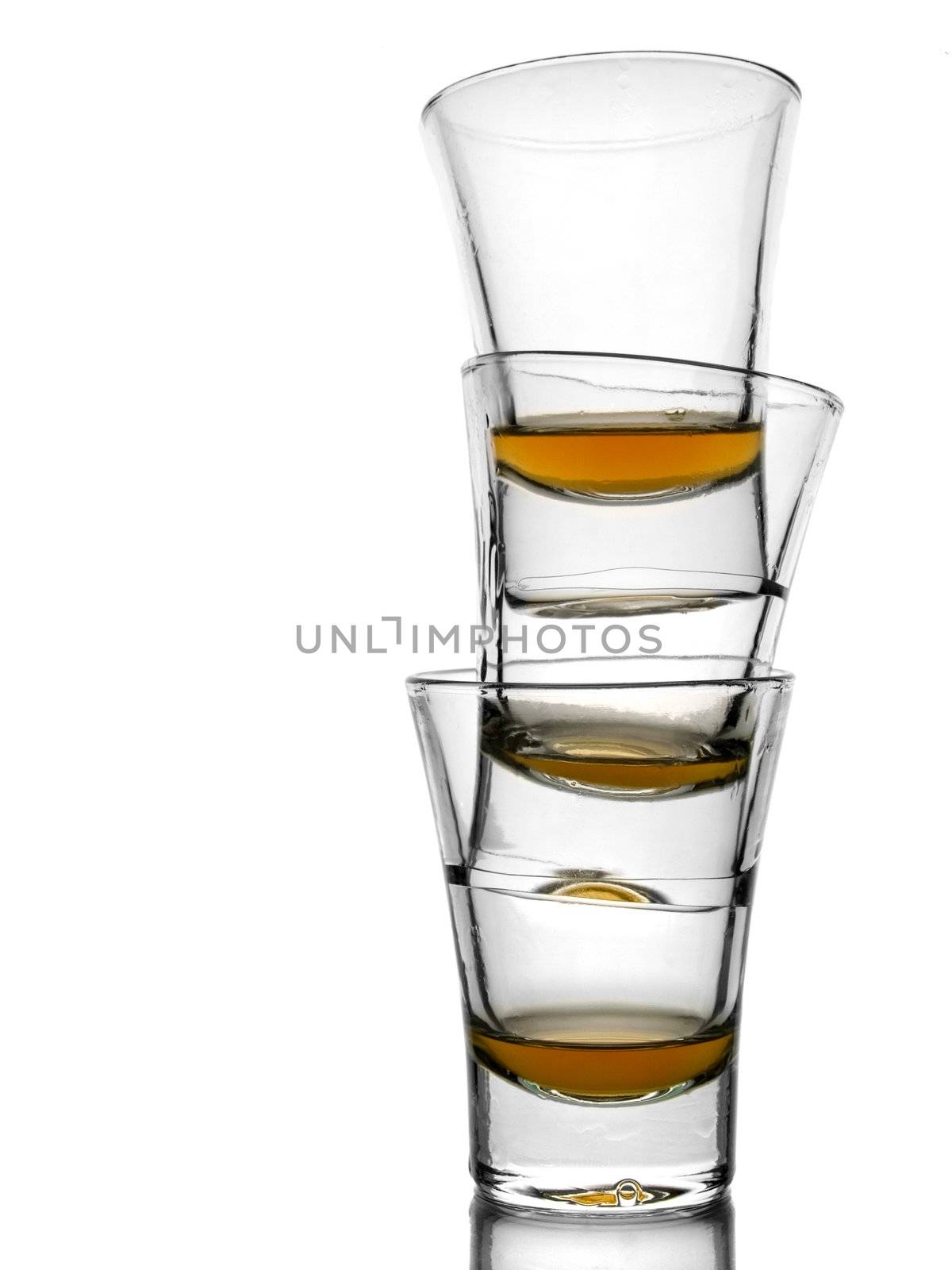 A pile of three almost empty shots of whisky on white background with reflex.