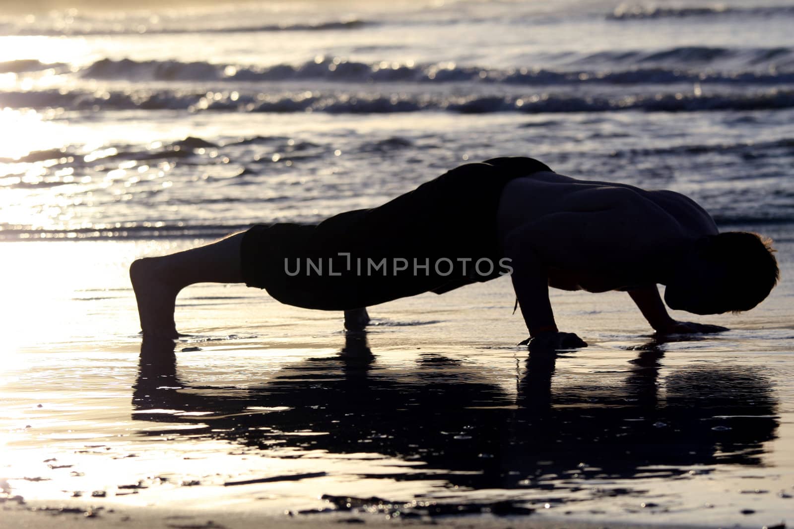 man doing press-ups on the beach by sunset