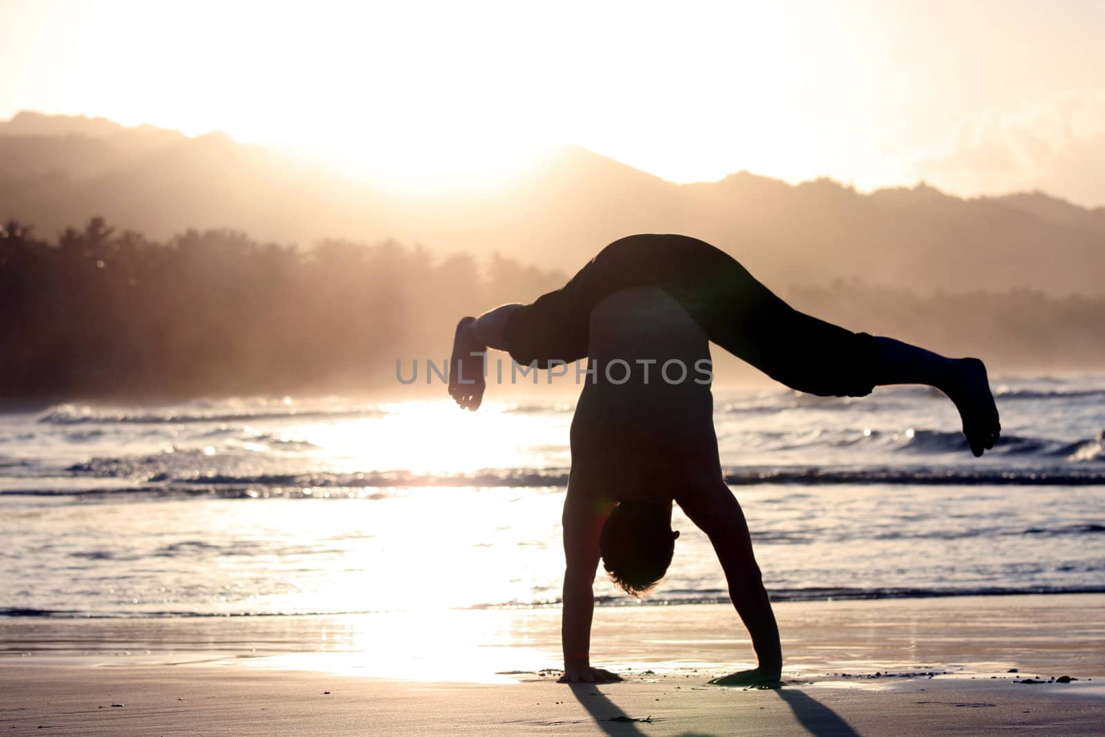 man trying to turn cartwheels on the beach by sunset