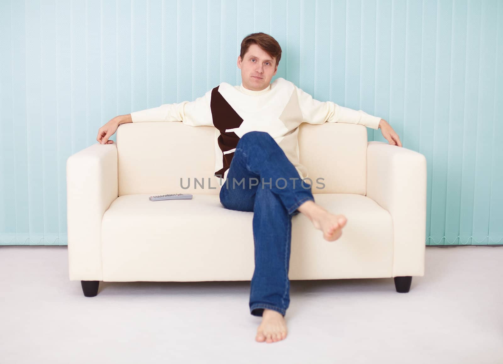 A young man sits comfortably on a soft sofa