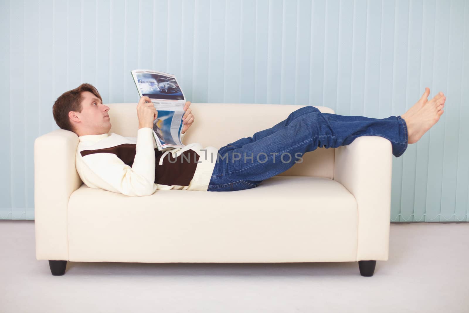 A young woman lies comfortably on a sofa with a newspaper