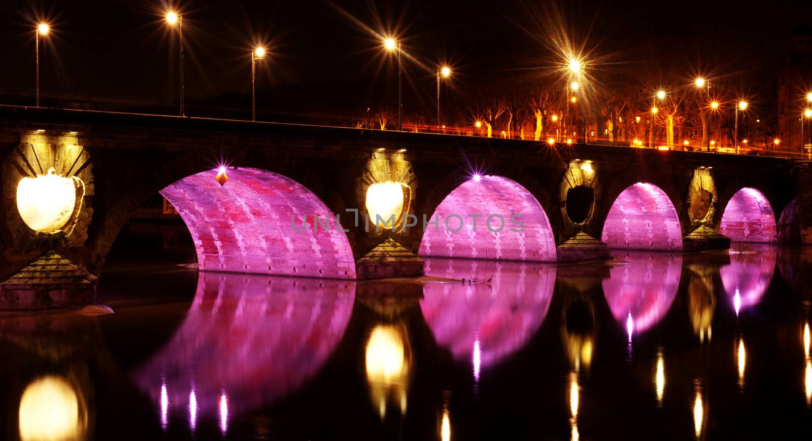 Pont neuf bridge illuminated at night with pink lights over the garonne in the city of Toulouse in France