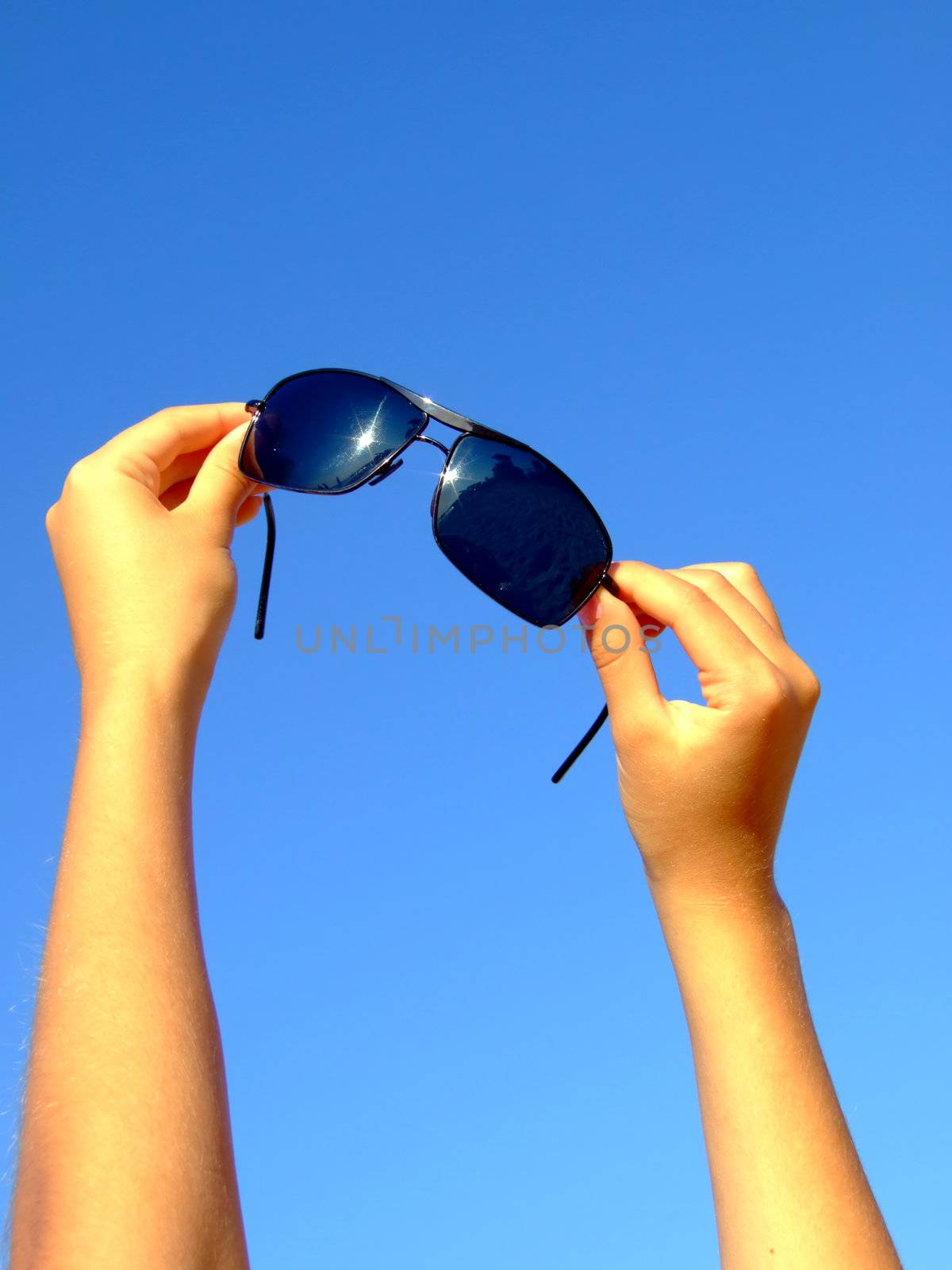 Female hands hold sunglasses on a background of the blue sky