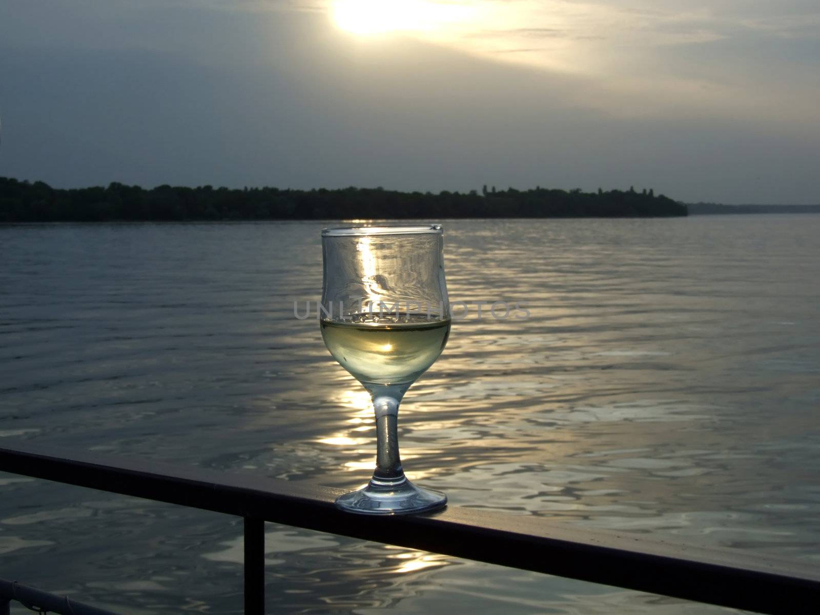 Glass of white wine on a background of a sunset above the river