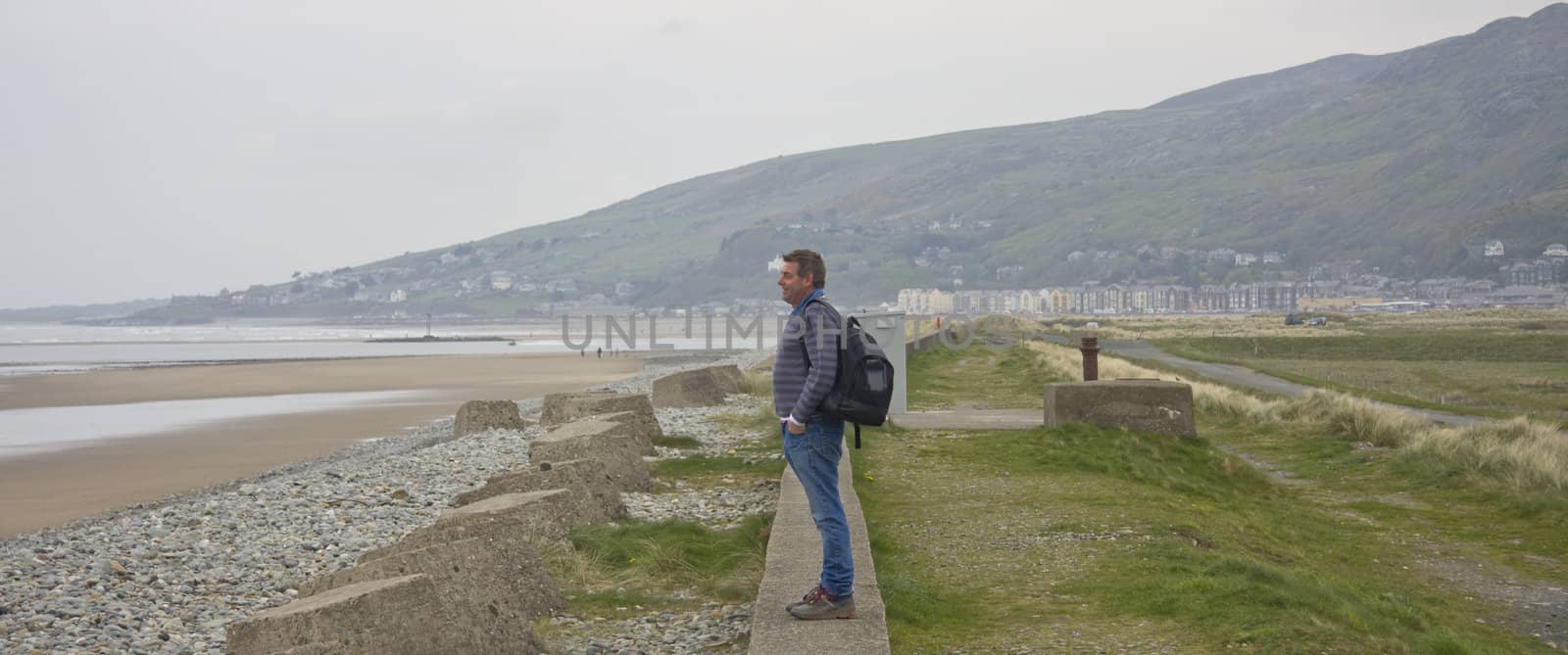 Man looking over an empty beach on a cloudy day.