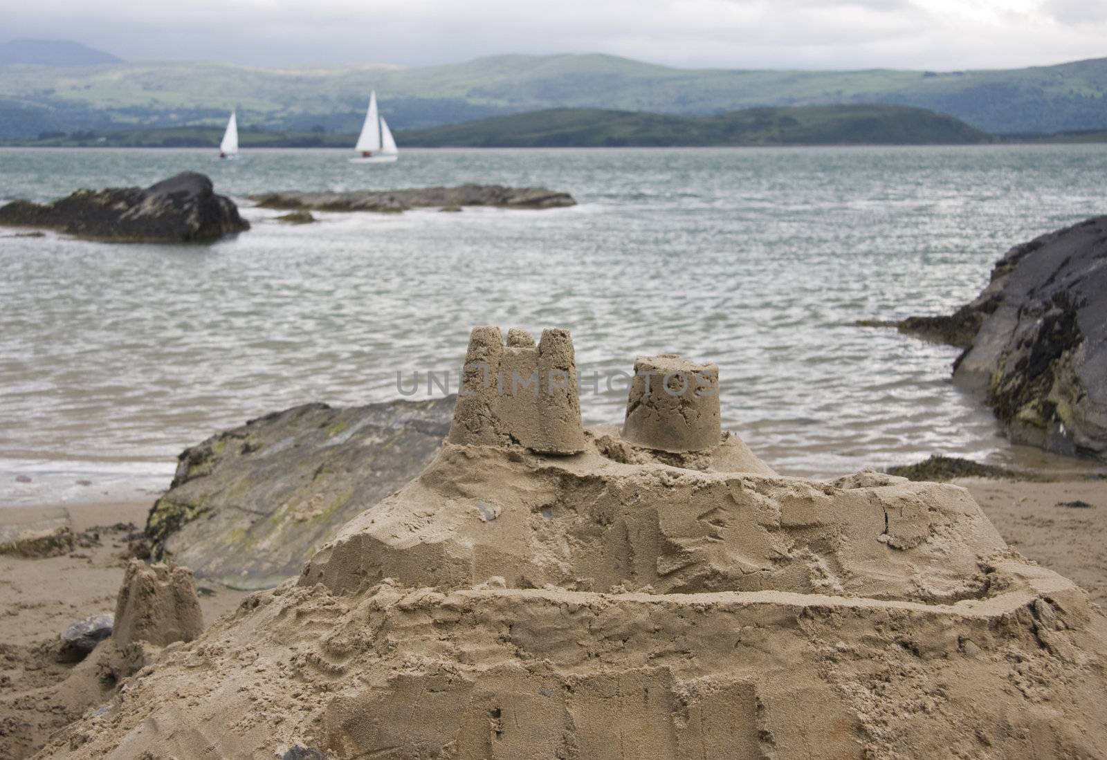 Sand castle on seas edge with two yachts sailing by.