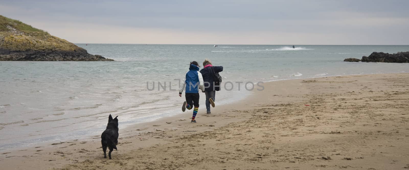 Two pretty girls running on the beach with thier dog by groomee