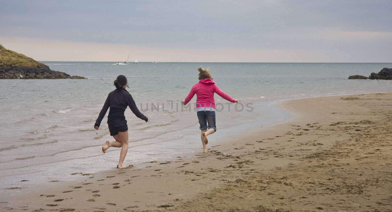 Two teenage girls run along the beach.
