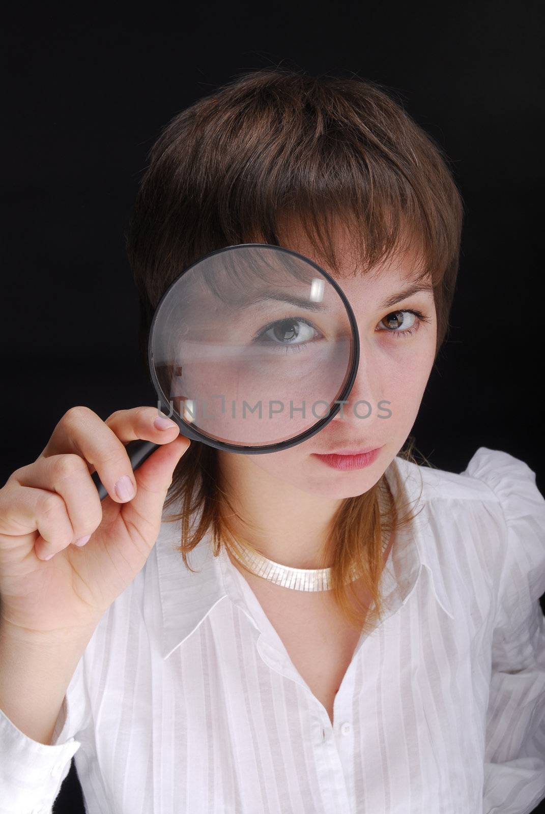 Young woman holding magnifying glass on black background