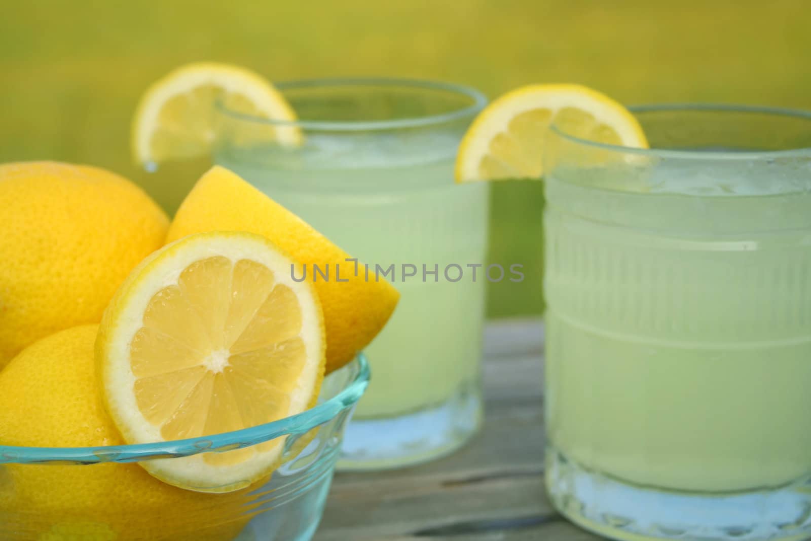 Two glasses of fresh lemonade and a bowl full of lemons outside on a summers day.