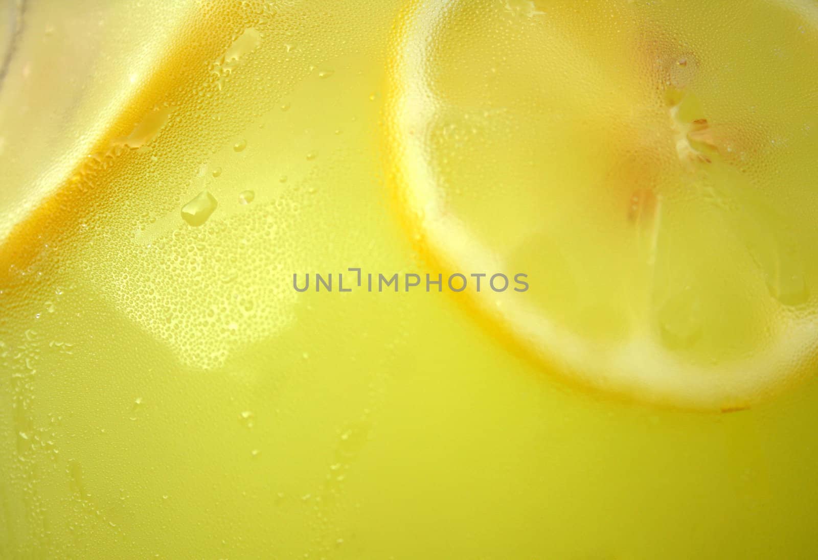 Close up of a pitcher full of lemonade with fresh lemons.  The glass pitcher has sweat beeds on it which adds texture.
