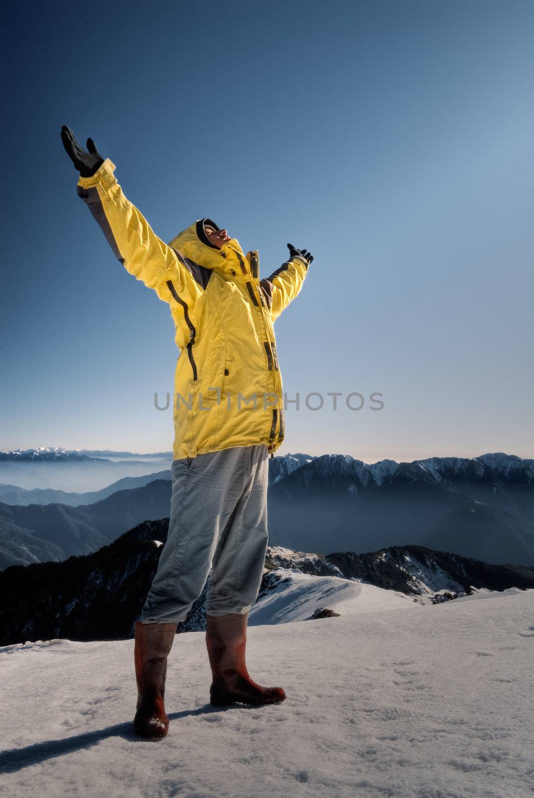 Man with open arms against blue sky on white snow hill.