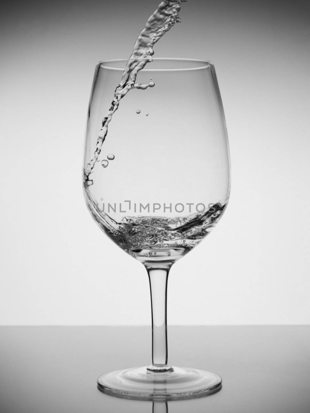 Water being poured into a glass with reflection on white background.