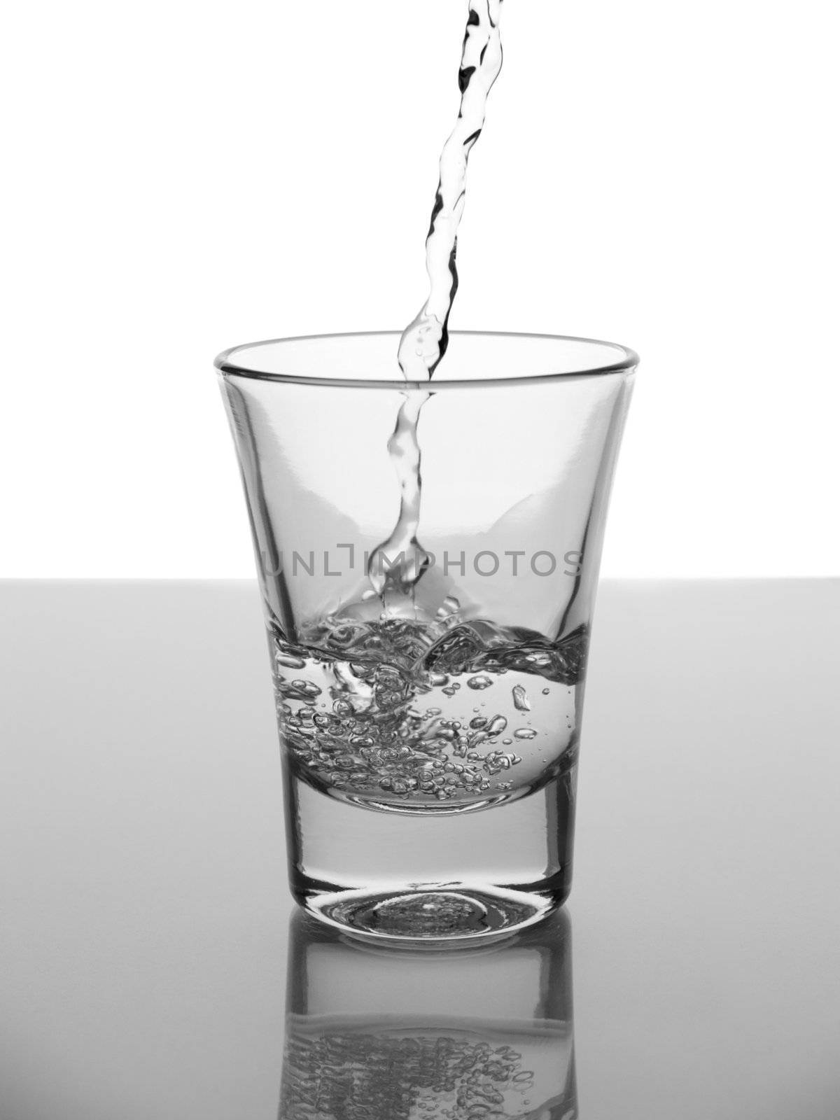 Water being poued into a glass with reflection on white background.