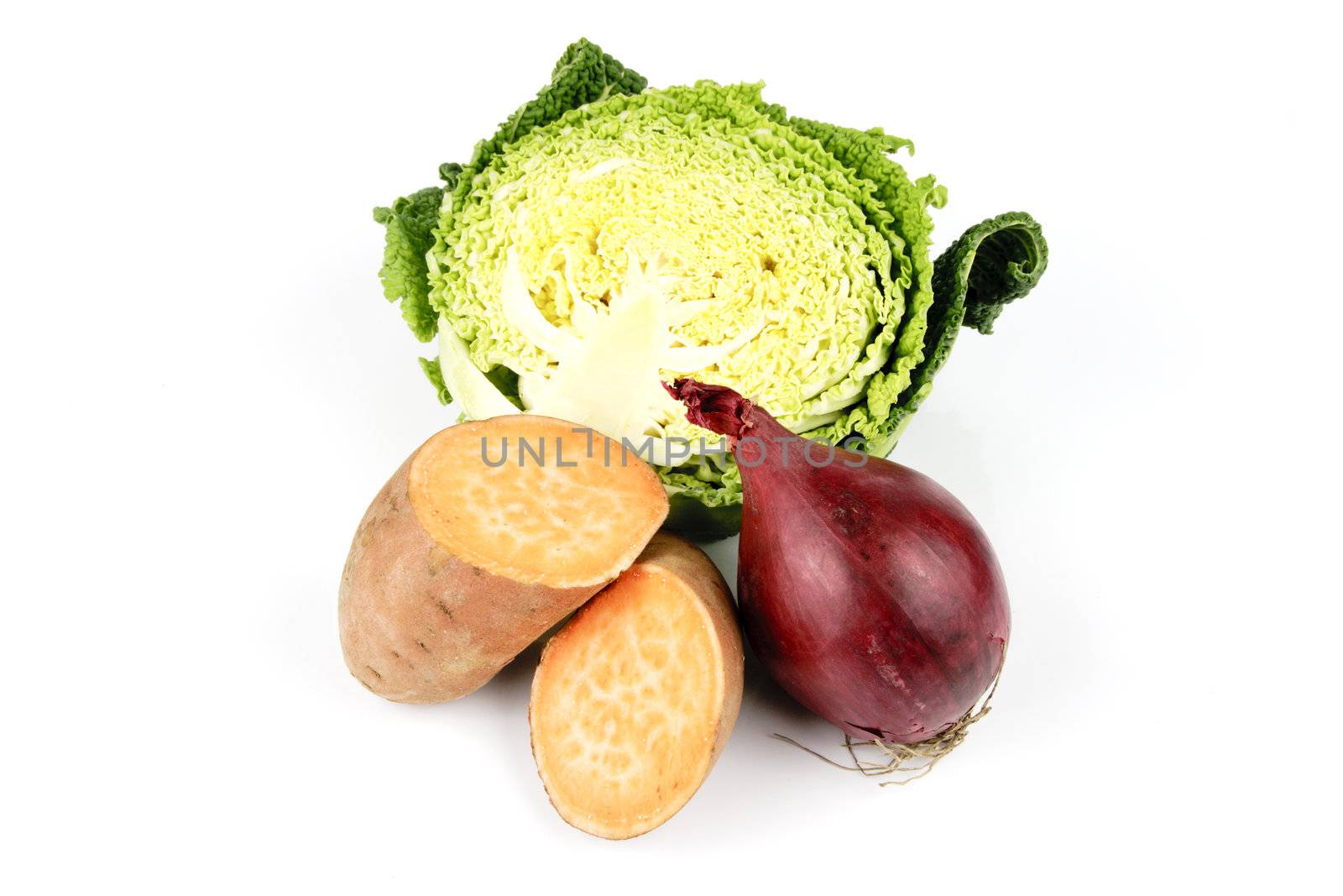 Half a raw green cabbage with a sweet potato cut in half and a single red onion on a reflective white background