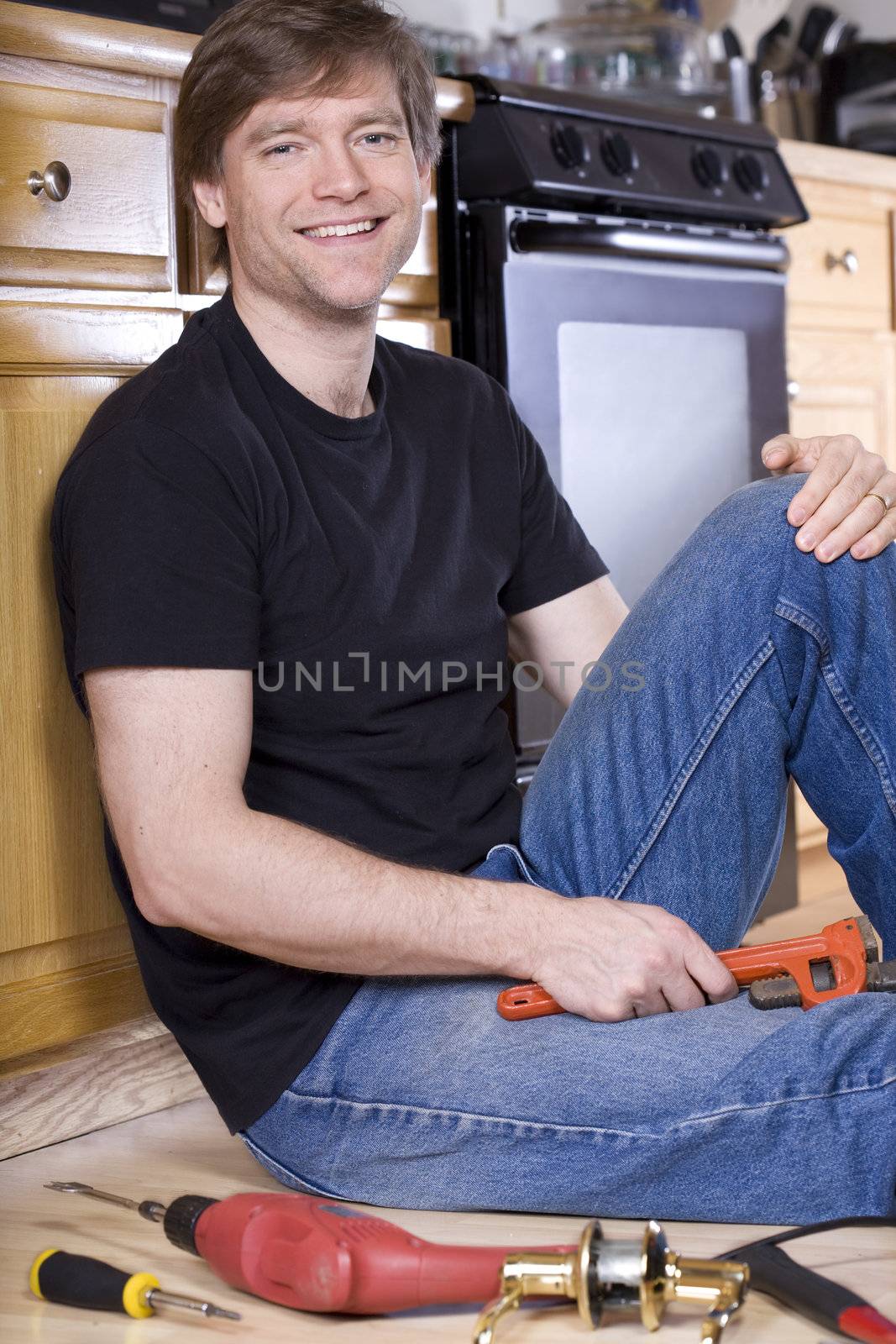 Handsome man sitting on floor of kitchen doing repairs