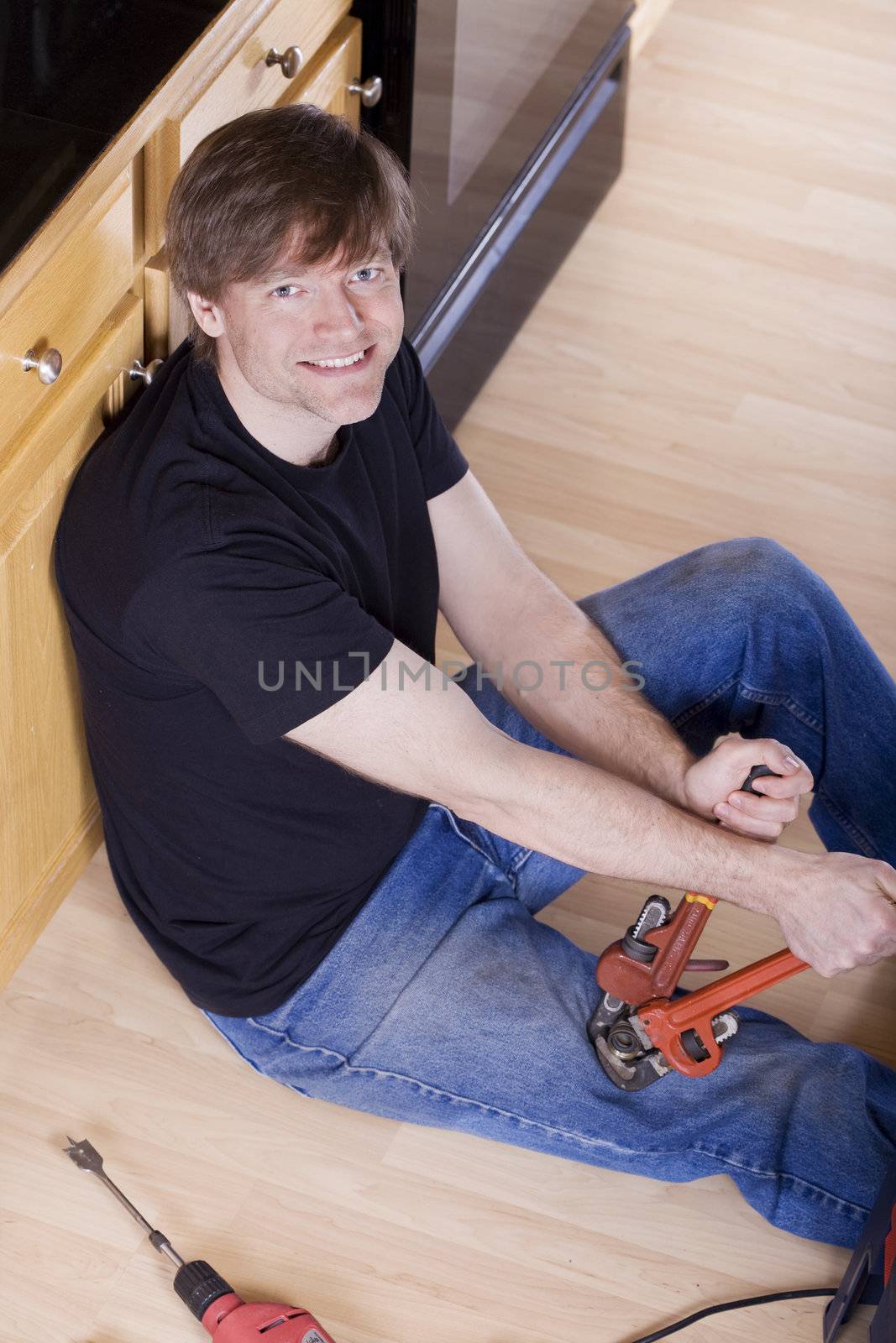 Handsome man in thirties sitting on kitchen floor doing repairs