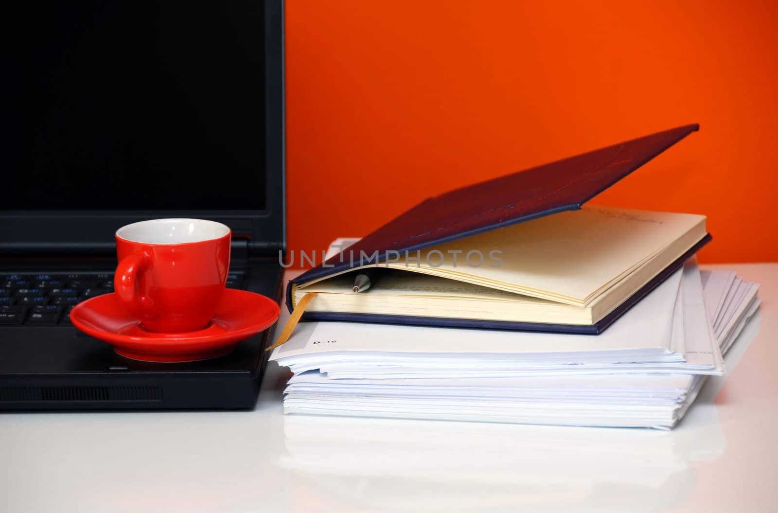 red cup over black notebook on office desk still life