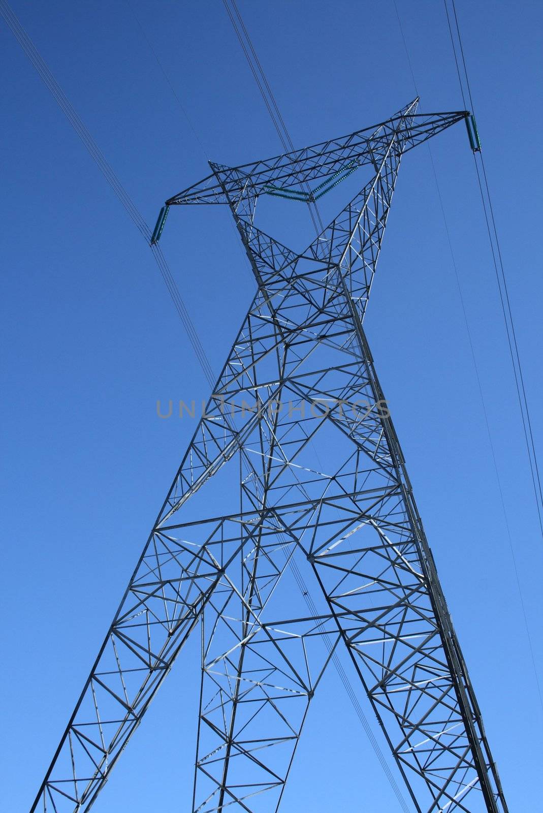 Silhouette of a high voltage electricity pylon against the deep blue sky.