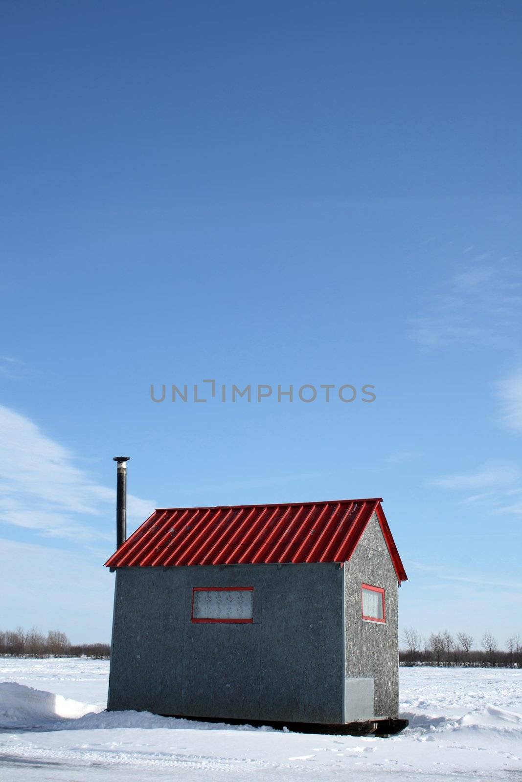 Ice fishing hut with red roof and chimney under the blue sky.