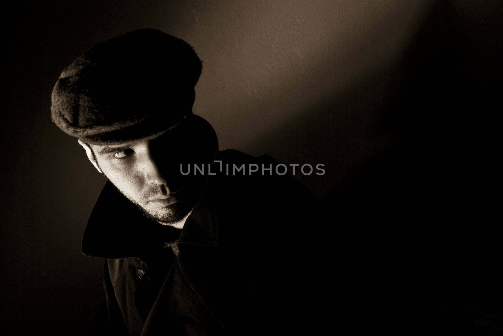 Sepia toned noir portrait of suspicious looking young man. Harsh highlights and shadows.