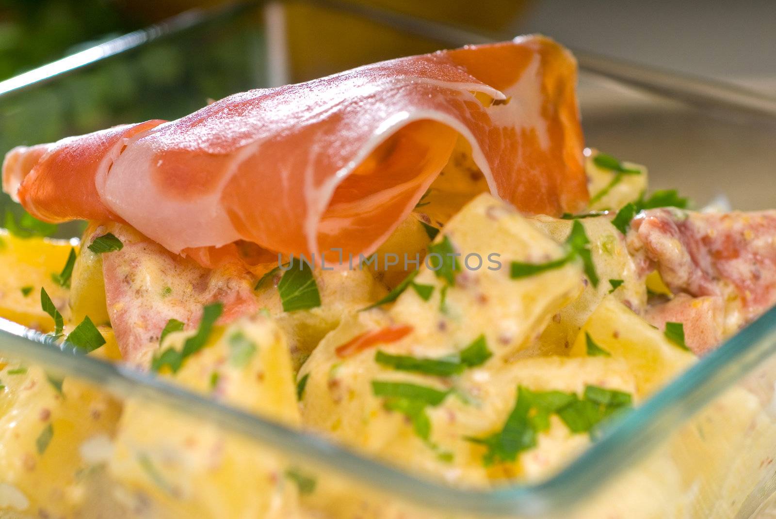 fresh home made parma ham and potato salad,with raw ingredients around with bowls and dishware on a table