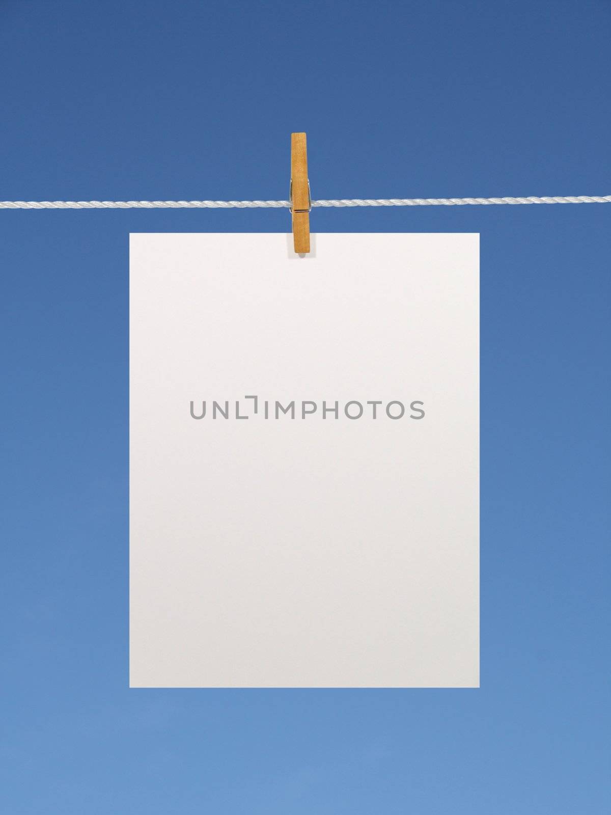 Blank paper sheet on a clothes line against the blue sky. Contains two clipping paths: 1) paper, clothes line and clothespin; 2) paper only