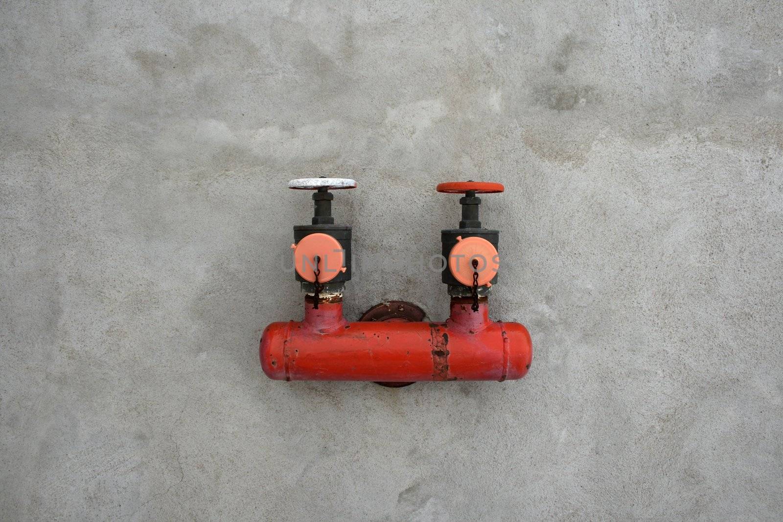 Red iron valve on a gray cement wall.