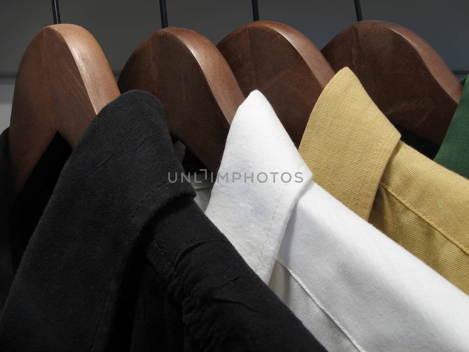 lack, white, yellow and green shirts on wooden hangers.